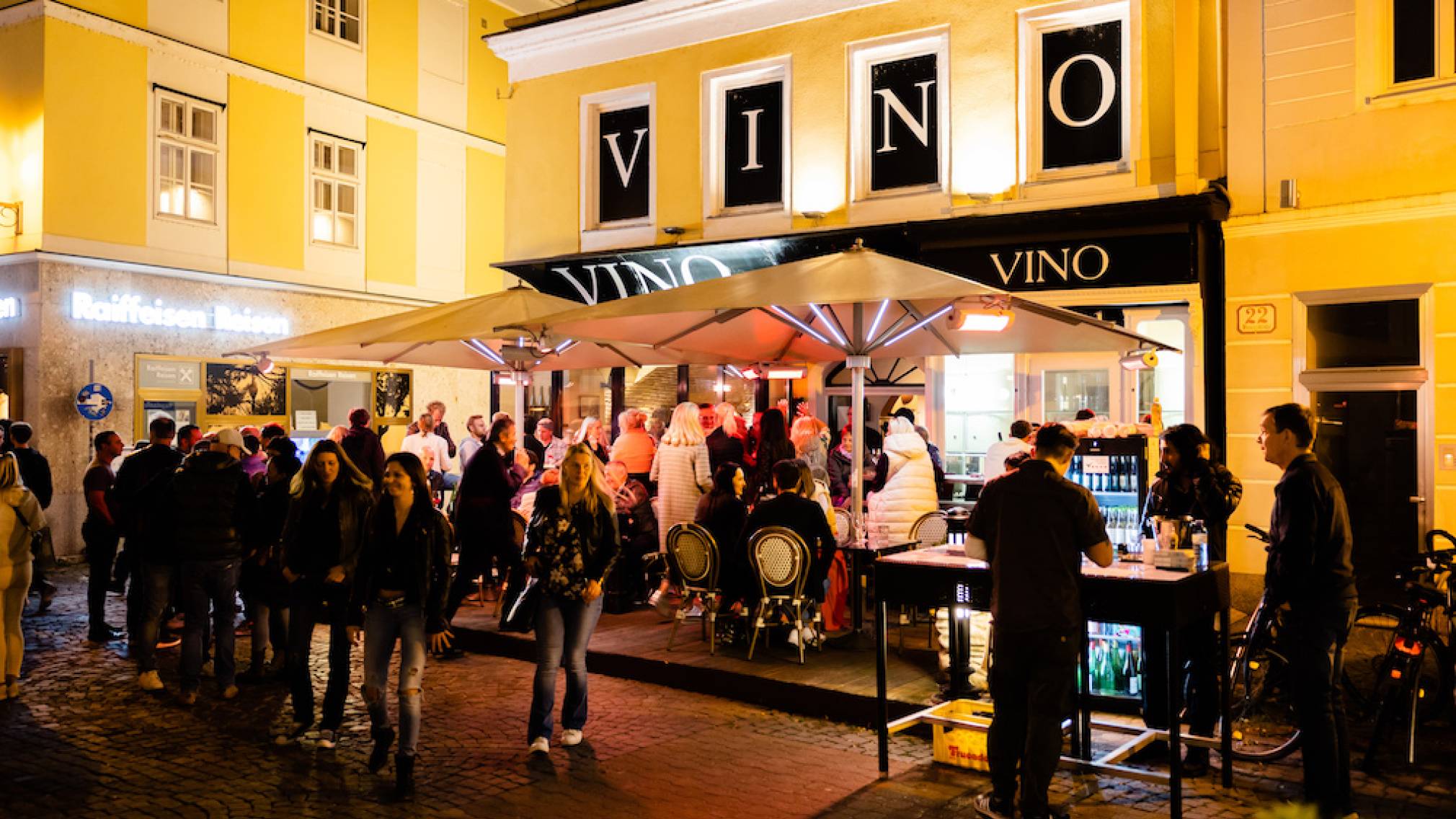 Zahlreiche Menschen stehen abends vor dem Weinlokal Vino in der schön beleuchteten St. Pöltner Innenstadt. Foto: Patrick Salfinger Fotografie